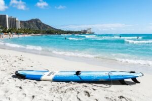 A longboard surfboard on a sunny beach in Waikiki Hawaii with ocean waves.