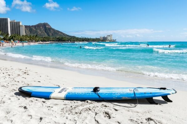 A longboard surfboard on a sunny beach in Waikiki Hawaii with ocean waves.